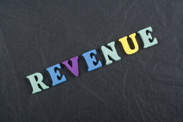 REVENUE word on black board background composed from colorful abc alphabet block wooden letters, copy space for ad text. Learning english concept.
