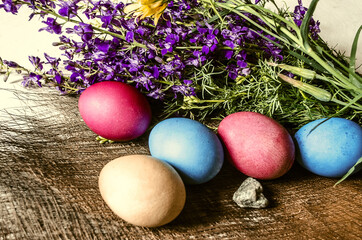 A bouquet of blooming purple wild flowers and painted Easter eggs on a straw mat

