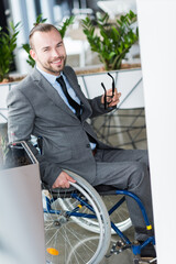 smiling physically handicapped businessman holding glasses and looking at camera