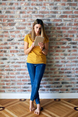 Young woman standing by the wall with tablet