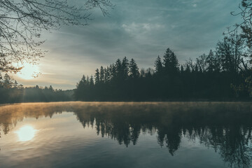 sunrise at lake with fog and reflections of sky and trees
