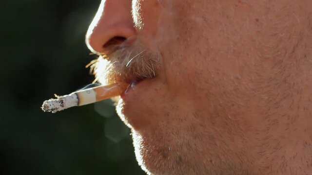 Close-up of mature man smoking cigarette, exhaling smoke outdoors