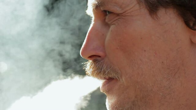 Face of mature man smoking cigarette, exhaling smoke outdoors