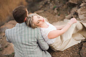 Love, romance and people concept - happy young couple hugging sitting on the edge of a cliff outdoors