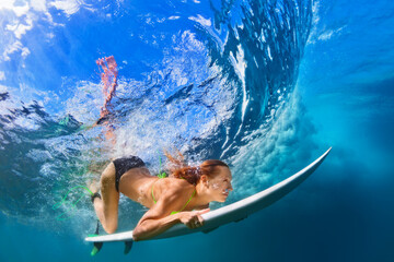 Active girl in bikini in action. Surfer woman with surf board dive underwater under breaking big...