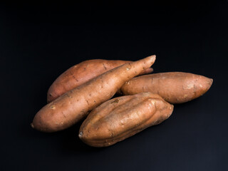 Heap of raw sweet potatoes isolated on black background