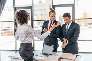 Young businesswoman gesturing and arguing with coworkers in office, business team meeting concept