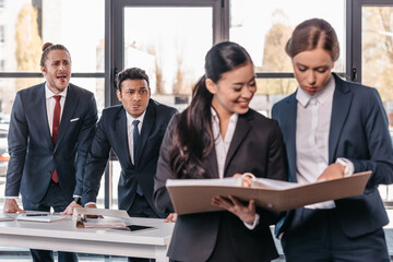 Young businesswomen working together while businessmen grimacing behind, business team working concept