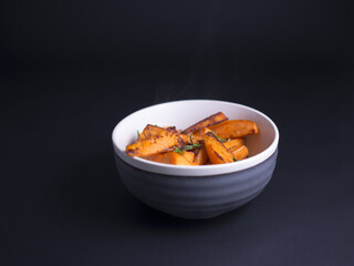 Fototapeta na wymiar Fried sweet potatoes wedges sprinkled with wild thyme and sea salt, served in rustic grey and white bowl on black background 