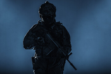 Army soldier in Protective Combat Uniform holding Special Operations Forces Combat Assault Rifle. Studio shot, silhouette