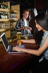 Woman having beer while using laptop at counter