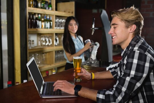 Man having beer while using laptop at counter