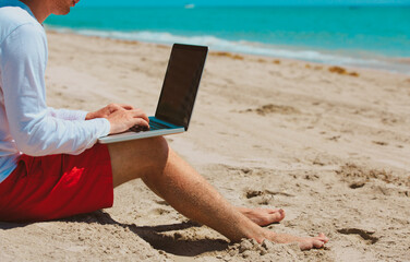 man working on laptop at tropical beach