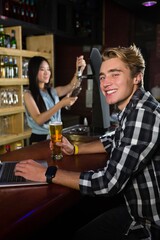 Man having beer while using laptop at bar counter