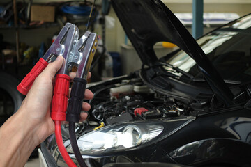 Hand holding Car battery charger over blurred car in garage background