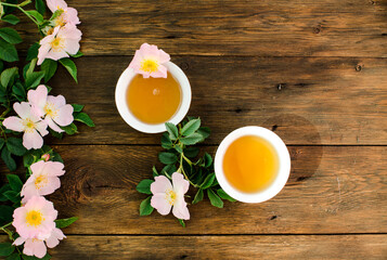 Cup of hot tea with rosehip and blooming flowers on old rustic wooden background