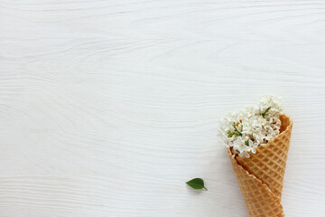 Summer ice cream/ Waffle horn with white lilac flowers and a green leaf lies on a white wooden table 