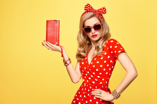 Fashion Model Girl in Polka Dots Summer Dress. Stylish Curly hairstyle, Trendy Clutch, fashion Red Headband, Sunglasses. Beauty Blond Pinup Woman in fashion pose. Glamour Playful Sexy Lady on Yellow