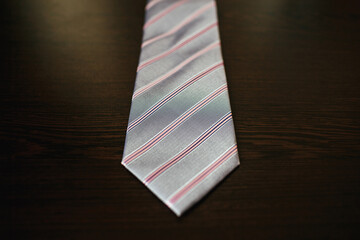 Grey tie with pink strips lies on wooden table