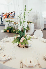 Bouquet made of roses and tall green branches stands in the center of dinner table