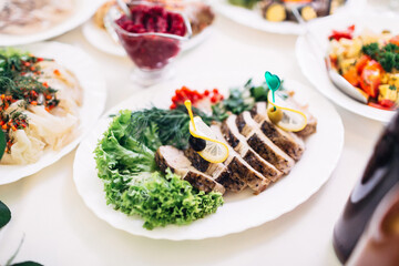 White dishes with greenery and fish stand on dinner table