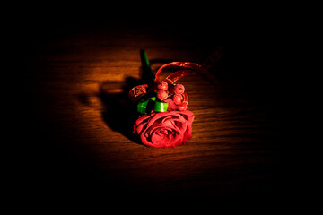 Boutonniere made of red rose and ribbon lies on wooden table