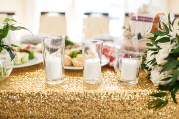 White candles stand on table covered with sparkling golden cloth