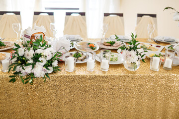 White candles stand on table covered with sparkling golden cloth