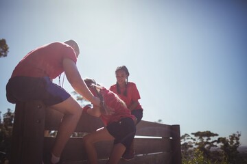 Trainer assisting kids to climb a wooden wall 