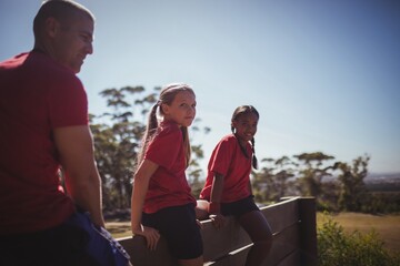 Fototapeta premium Trainer and girls sitting together on a wooden wall