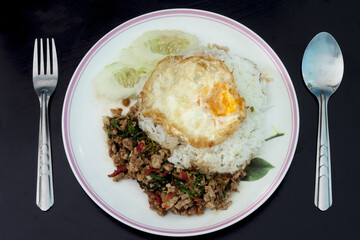 Basil Pork with Egg with Cutlery on wood black color.