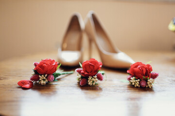 Red boutonnieres lie before beige shoes on wooden floor