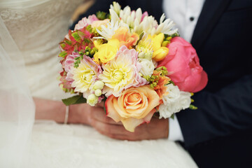 Bride and groom hold colorful wedding bouquet in their arms