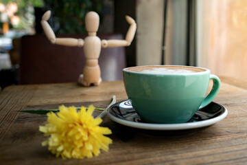 Hot mocha coffee or capuchino with yellow flower and wood man on the wooden table