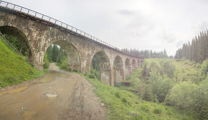 Fototapeta na wymiar Old stone railroad bridge among fir trees