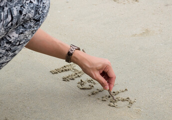 A lady's hand writing word 'HELLO' on the sand at the beach