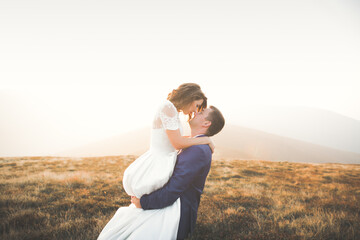 Naklejka na ściany i meble Beautiful wedding couple posing on top of a mountain at sunset