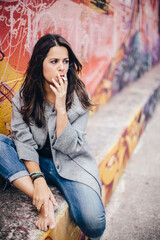 Fototapeta na wymiar Young pretty woman smoking near a colorful wall with a thoughtful expression. Lifestyle portrait outdoors.