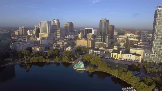 Aerial reveal flying backwards over Lake Eola amphitheater in downtown, Orlando, FL in early morning.