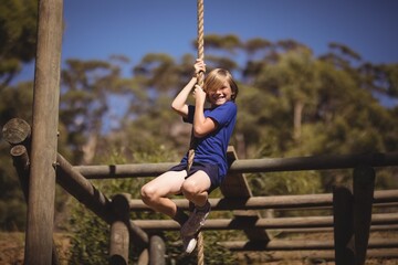 Portrait of smiling girl climbing rope during obstacle course