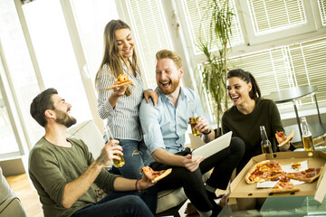 Young people eating pizza, drinking cider and watching tablet in the room