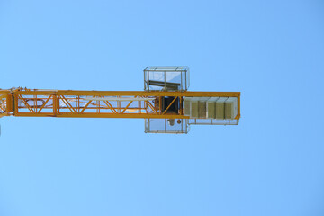 Yellow tower crane against blue sky on construction site.