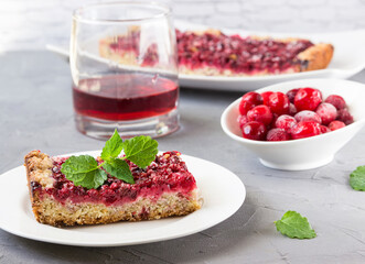 A piece of pie with cowberry, mint, cranberry juice on the table.