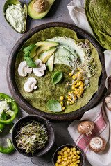 Green spinach matcha tortilla with vegan ingredients for filling. Sweet corn, avocado, green paprika, sprouts, mushrooms served in terracotta plate over gray texture background and textile. Flat lay