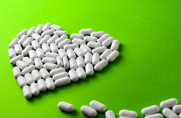 white heart made of pills on a green background.