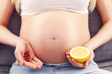 Pregnant woman holding pills and lemon at home