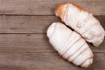 two croissants sprinkled with powdered sugar on old wooden background with copy space for your text. Top view