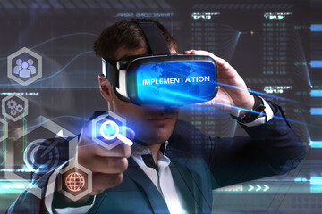 Business, Technology, Internet and network concept. Young businessman working in virtual reality glasses sees the inscription: Implementation