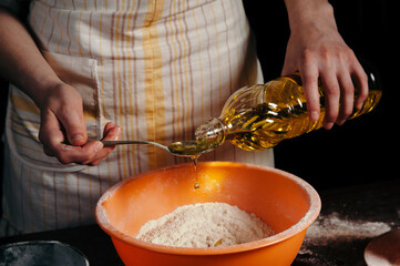 Female hand pour sunflower oil in a bowl with the flour. Preparation of the test. A drop of oil. Beautiful.