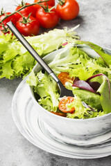 The dietary mixed greens salad (mesclun, mache, lettuce) and cherry tomatoes in a bowl on a light background